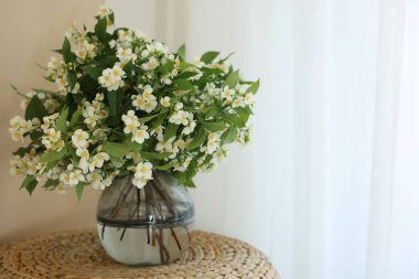 Güzel yasemin çiçekleri vazonun içinde pencerenin yanındaki hasır masada, metin için yer var.