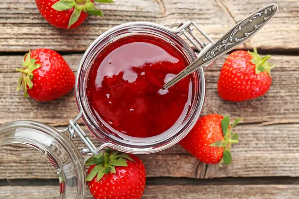 Cam kavanozda çilek reçeli ve ahşap masada taze böğürtlen.