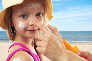 Anne sahilde kızının yüzüne güneş kremi sürüyor, yakın plan. Yazın dışarıda dinlenirken güneş koruması