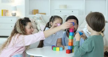 Çocuklar ve aileleri beyaz masa içinde renkli küplerle kule inşa ediyorlar.