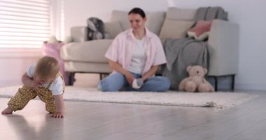 Anne, sevimli bebeği evde yerde, seçici bir şekilde odaklanmış. Kamera sola hareket ediyor