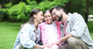 Aile hafta sonu. Mutlu ebeveynler parkta kızlarını öpüyor.