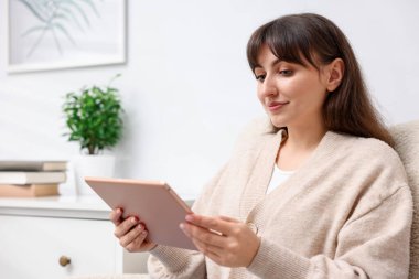 Evdeki koltukta modern tablet kullanan bir kadın. Metin için boşluk