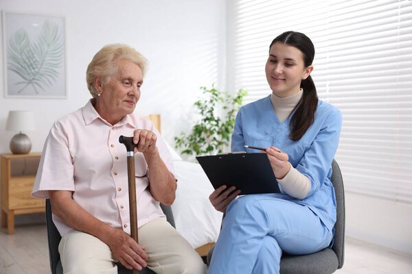Nurse with clipboard examining senior woman indoors. Home health care service
