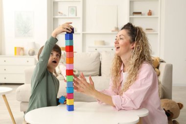 Anne ve oğlu beyaz masada tahta küplerle kule inşa ediyorlar.