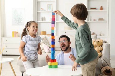 Çocuklar ve babaları beyaz masada renkli küplerle kule inşa ediyorlar.