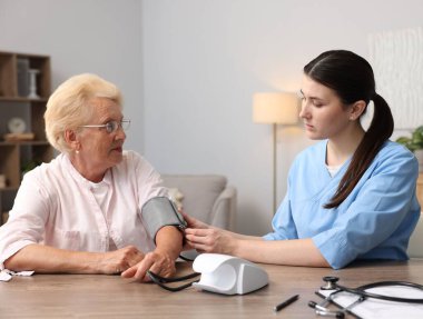 Hemşire, içeride ahşap masada hastanın kan basıncını ölçüyor. Ev sağlık hizmetleri