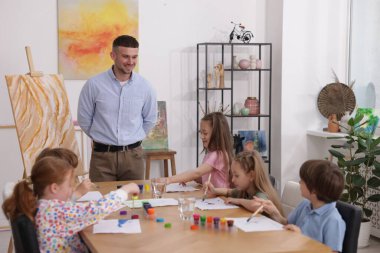 Çocuklara resim dersinde resim yapmayı öğreten bir adam.