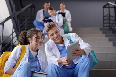 Bir grup tıp öğrencisi merdivenlerde kapalı, düşük açılı üniformalarla.