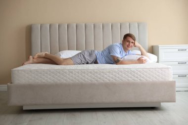 Genç adam evde yumuşak bir döşekle yatakta yatıyor.