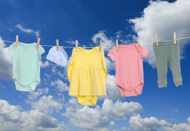 Mavi gökyüzüne karşı çamaşır ipinde kurumuş farklı bebek kıyafetleri.