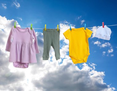 Mavi gökyüzüne karşı çamaşır ipinde kurumuş farklı bebek kıyafetleri.