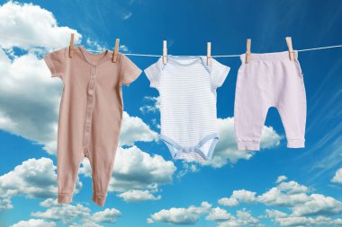 Mavi gökyüzüne karşı çamaşır ipinde kurumuş farklı bebek kıyafetleri.