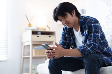 Evdeki kanepede akıllı telefonlu yakışıklı Asyalı adam. Metin için boşluk