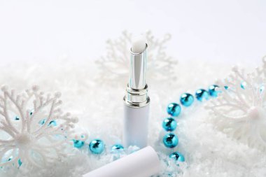 Nemlendirici dudak kremi ve yapay kar üzerine Noel süsü, yakın plan. Kış bakımı