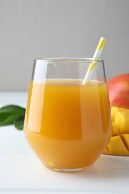 Lezzetli mango suyu bardakta, taze meyve ve yeşil yapraklar beyaz ahşap masada, yakın plan