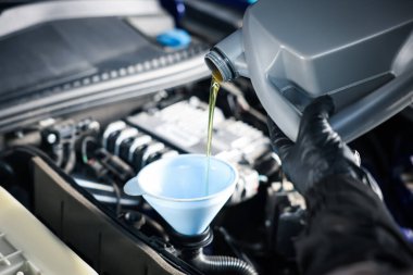 İşçi motor yağını teneke kutudan araba motoruna boşaltıyor.