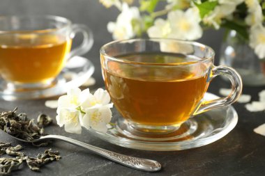 Aromatik yasemin çayı, bira ve çiçekler gri masada, yakın plan.