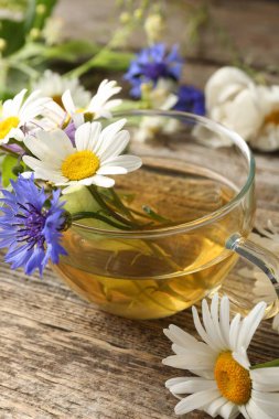 Cam bardakta Aromatik bitki çayı ve ahşap masada çiçekler, yakın plan.