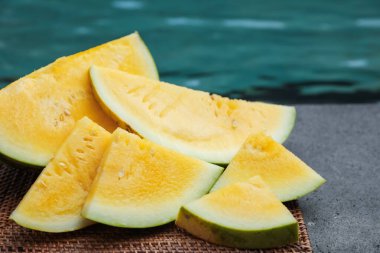 Yüzme havuzunun yanındaki masada olgun sarı karpuz parçaları, yakın plan.