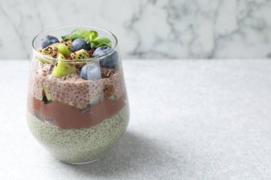 Chia tohumlu çikolatalı puding, kivi, nane ve böğürtlenli cam, gri desenli masada mermer arka planda, yakın plan. Metin için boşluk