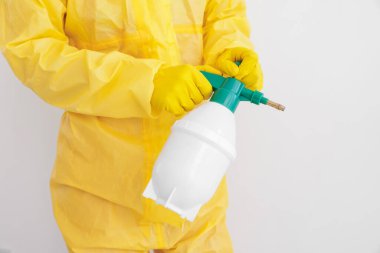 Koruyucu kıyafetli haşereci beyaz duvarın yakınına böcek ilacı sıkıyor.