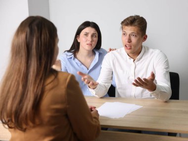 Ahşap masadaki kadına şikayet eden bir çift.