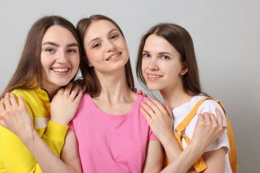 Arkadaşlar açık gri arka planda birbirlerine sarılıyorlar.