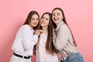 Arkadaşlar pembe arka planda birbirlerine sarılıyorlar.