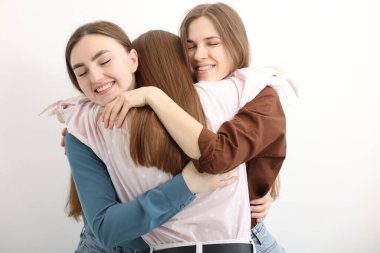 Arkadaşlar beyaz arka planda birbirlerine sarılıyorlar.