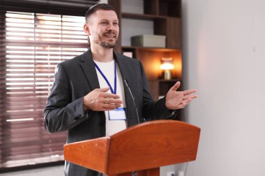 İçerideki kürsüde mikrofonla halka açık konuşma yapan adam.