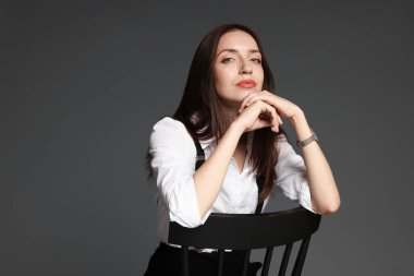 Şık giyinmiş güzel bir kadın gri arka planda sandalyede oturuyor, mesaj için yer var.