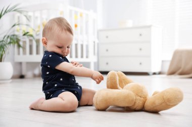 Küçük şirin bebek odada oyuncak ayıyla oynuyor.