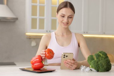 Beyaz masadaki akıllı telefon ve domatesli kadın.