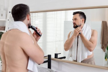 Yakışıklı adam banyoda aynanın yanında tıraş makinesiyle tıraş oluyor.