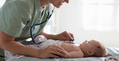 Klinikteki masada steteskopla bebeği muayene eden çocuk doktoru.