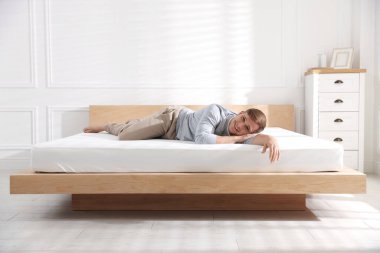 Genç adam evde yumuşak bir döşekle yatakta yatıyor.