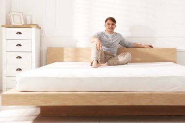 Genç adam evinde yumuşak bir yatakla yatakta oturuyor.