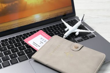 Pasaport, uçuş bileti, uçak modeli ve laptop beyaz ahşap masada, yakın plan.