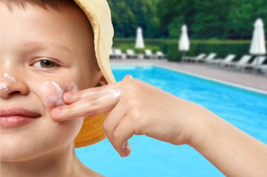 Küçük çocuk dış yüzme havuzunda yüzüne güneş koruması uyguluyor.