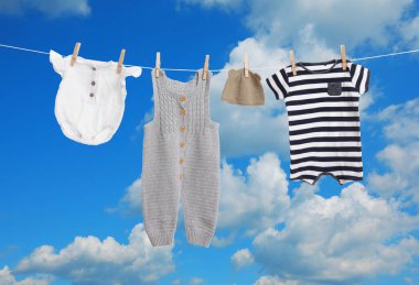 Mavi gökyüzüne karşı çamaşır ipinde kurumuş farklı bebek kıyafetleri.