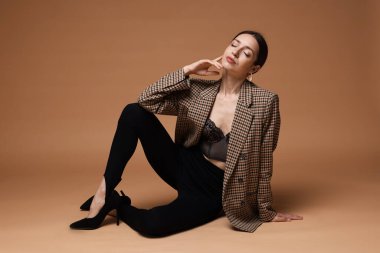 Bej arka planda şık giyinmiş güzel bir kadının tam boy portresi.