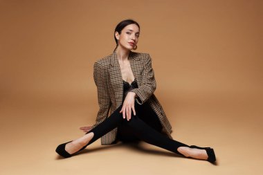 Bej arka planda şık giyinmiş güzel bir kadının tam boy portresi.