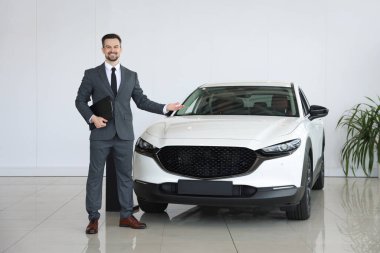 Elinde dosya olan gülümseyen satıcı kuaförde yeni bir araba gösteriyor.