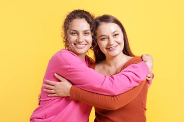 Arkadaşlar turuncu arka planda birbirlerine sarılıyorlar.