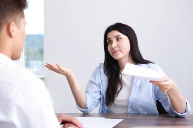 Genç bir kadın içerideki ahşap masadaki adama şikayette bulunuyor.