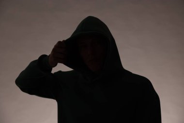 Gri arka planda kapüşonlu isimsiz bir adamın silueti.