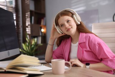 Kulaklık takmış genç bir öğrenci içeride ders çalışıyor.