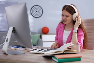 İçeride ders çalışırken kulaklıklı bir öğrenci bilgisayar kullanıyor.