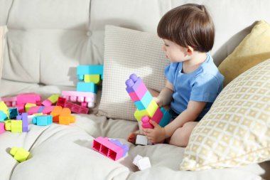 Evdeki kanepede tuğlalarla oynayan şirin bir çocuk.